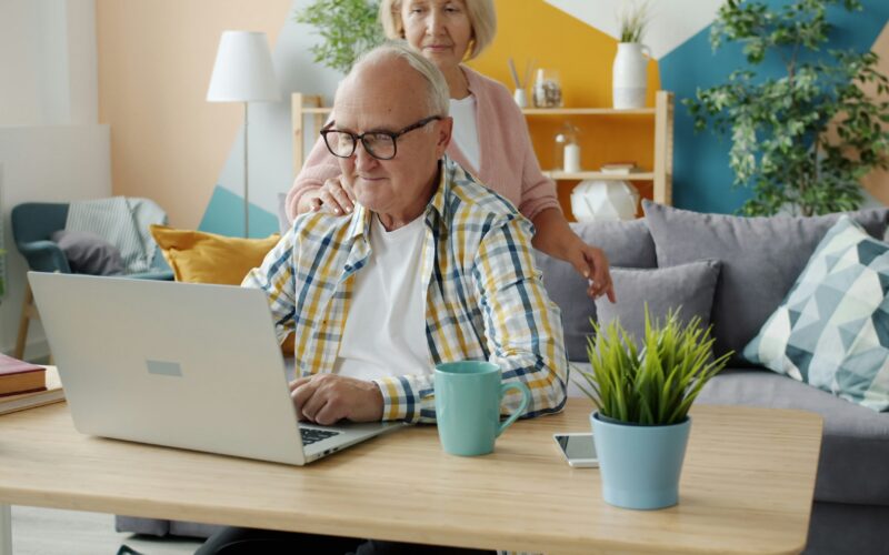 SENIOR COUPLE WORKING AT HOME ON LAPTOP